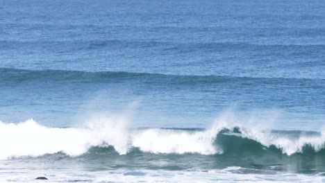 Grandes-Líneas-De-Oleaje-Llegan-A-La-Orilla-Y-Rompen-En-La-Costa-Con-Un-Océano-Azul