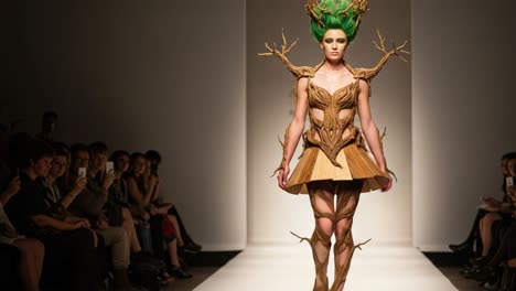 a stunning model showcases an innovative nature-inspired fashion design with unique wood and leaf elements on the runway, captivating the audience's attention with artistic flair