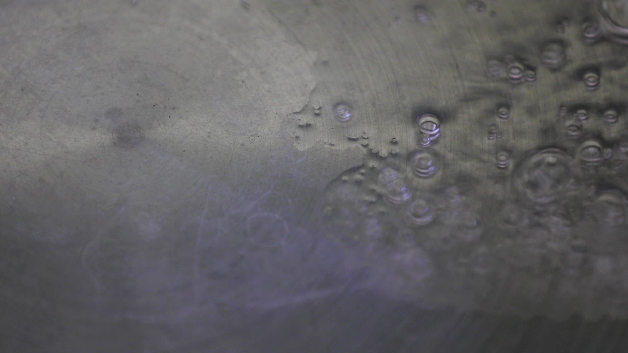una vista de cerca captura el momento de verter agua en una sartén caliente, con pequeñas burbujas que salen