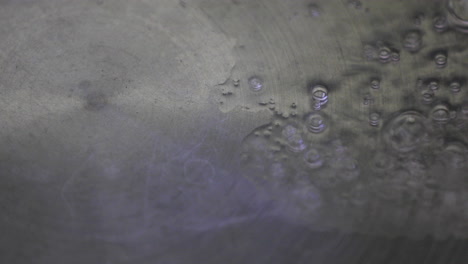 close-up view captures the moment of pouring water into a hot pan, with tiny bubbles popping up