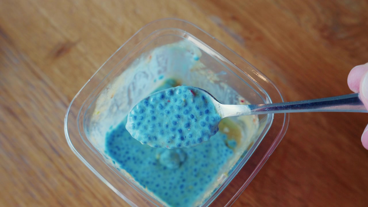 Primo piano di budino di semi di chia in un contenitore di vetro, con un cucchiaio che solleva la miscela blu testurizzata.