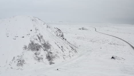 AERIAL:-Towards-Snow-White-Mountain-with-Black-Rocks-in-Iceland-Winter,-Snowing,-Cold,-Arctic