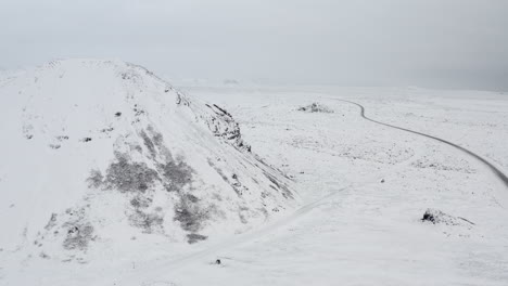 Aéreo:-Hacia-La-Montaña-Blanca-Como-La-Nieve-Con-Rocas-Negras-En-Islandia-Invierno,-Nevando,-Frío,-ártico