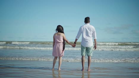 Toma-En-Cámara-Lenta-De-Una-Pareja-En-Una-Playa-De-Pie-Y-Mirando-Las-Hermosas-Olas