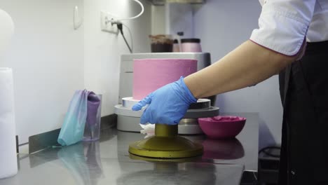 Spinning-a-purple-cake-on-special-tray-while-finishing-up-decorating-it.-Taking-extra-whipped-cream-off-bottom.-Confectioner-food-art.-Making-delicious-dessert.