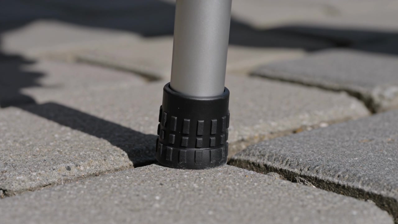 Contacting aluminum leg settling, rotating compressing rubber foot into paver joint, stabilizing