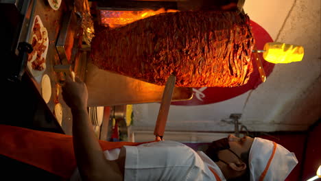 vertical slow motion of a latin male cook cutting meat from a "trompo de pastor" to make classic mexican tacos at a restaurant in mexico city