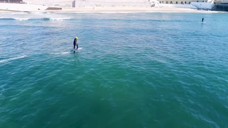 athlete on a hydrofoil surfboard riding a wave, using a foil drive assist pumps to catch a wave on the outside.