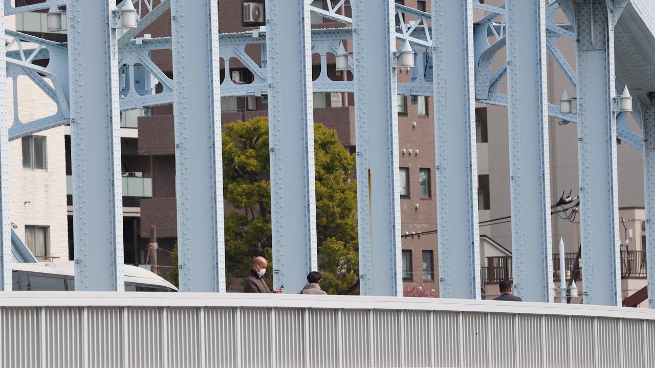 Peatones caminan junto a vigas de acero industriales azules en un puente urbano en Tokio, Japón