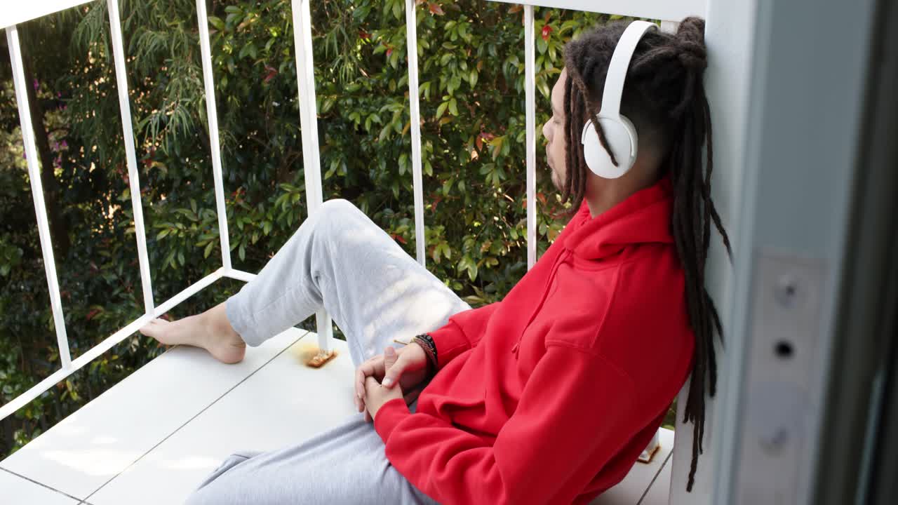 Uomo che esce sul balcone, preme play sullo smartphone, ascolta musica e guarda il fogliame.
