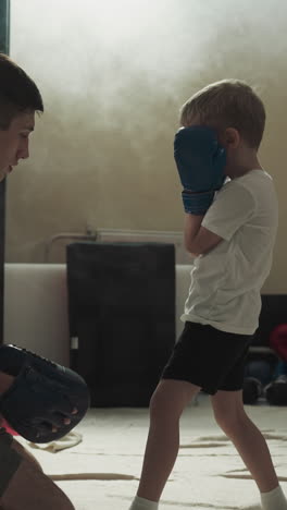el instructor muestra la posición de las piernas al niño en el gimnasio deportivo. el entrenador de artes marciales enseña al niño a pelear boxeo en cámara lenta del club. desarrollo de los niños