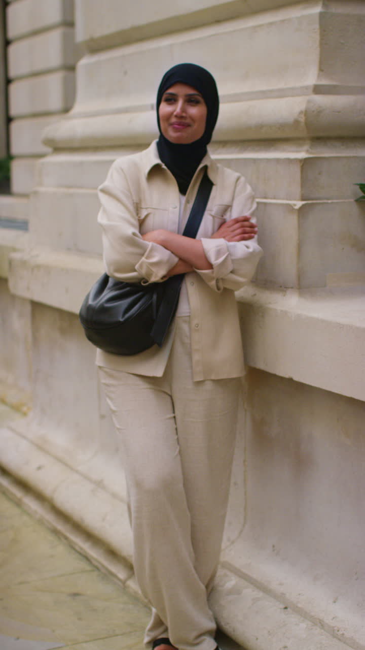 Vertical Video Portrait Of Smiling Muslim Businesswoman Wearing Hijab And Modern Business Suit Standing And Folding Arms Outside City Office Buildings 3