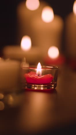 vertical video close up of romantic lit red and white candles burning on black background with bokeh lighting 5