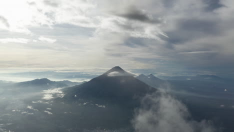 panorámica aérea de conos de montañas volcánicas que se elevan desde el centro del paisaje en las nubes