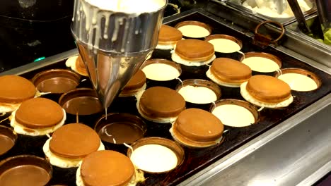 making delicious obanyaki or imagawayaki by drop the young bread into a hot pan stuffed with cream custard and other. traditional japanese snack is popular.