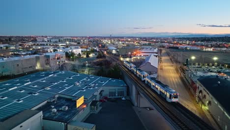 Public-transportation-trains-pass-each-other-on-rail-tracks-at-dusk-during-evening-commute,-aerial-overview