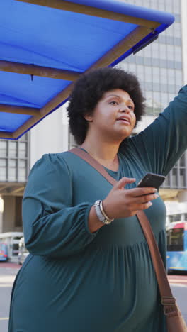 vertical video of plus size biracial woman walking on street with smartphone