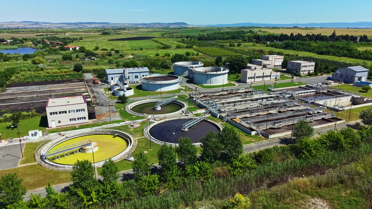 Wastewater treatment facility in a rural area with tanks and machinery under clear sky