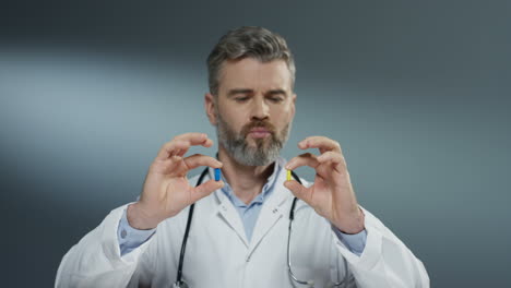 lindo médico masculino sosteniendo dos pastillas en las manos amarillas y azules y mirándolas como comparar y elegir una azul