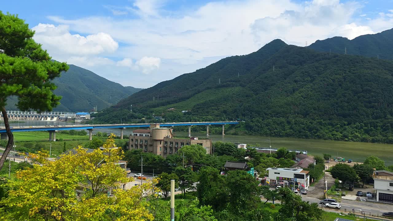 An aerial panorama soars above the Bukhangang River in Gapyeong, capturing bustling traffic on the Sincheongpyeongdae Bridge and the impressive Cheongpyeong Dam nestled among verdant mountains
