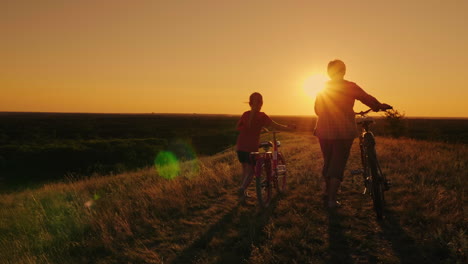 back view: an elderly lady walks with her granddaughter bicycles at sunset