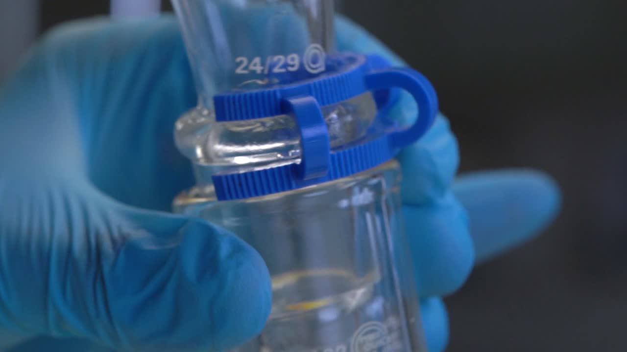 primer plano de un químico que usa una columna de embudo de caída para mezclar soluciones