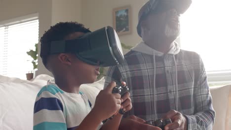 abuelo y nieto afroamericanos sentados en el sofá, usando auriculares vr, cámara lenta