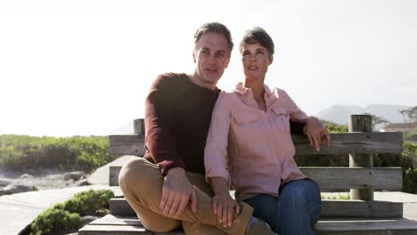 Caucasian-couple-enjoying-free-time-by-sea-on-sunny-day-sitting-on-bench