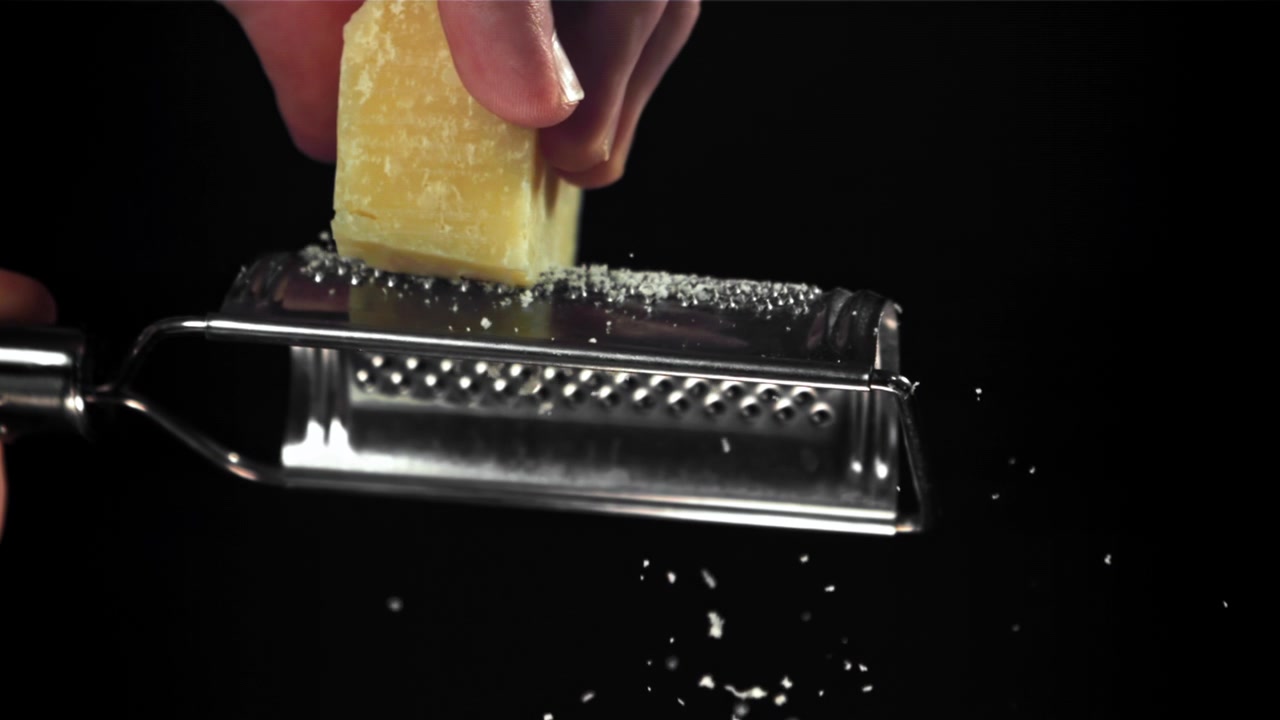 Primo piano di una mano che grattugia Parmigiano Reggiano al rallentatore
