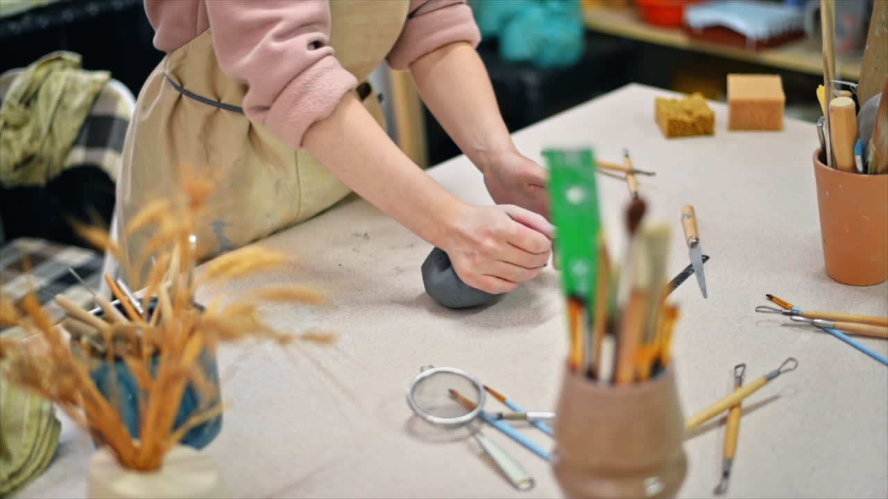 The master of sculpting pottery working in a studio. Kneading a piece of clay with her hands. Tools on the table. Slow motion