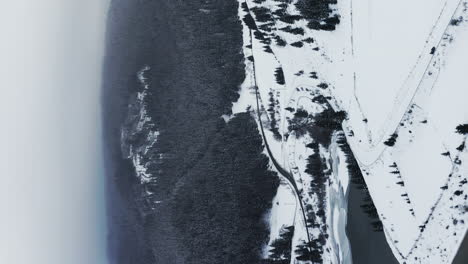 Vertical-flyover-above-Frumoasa-Dam,-Romania-during-winter,-blanketed-with-snow