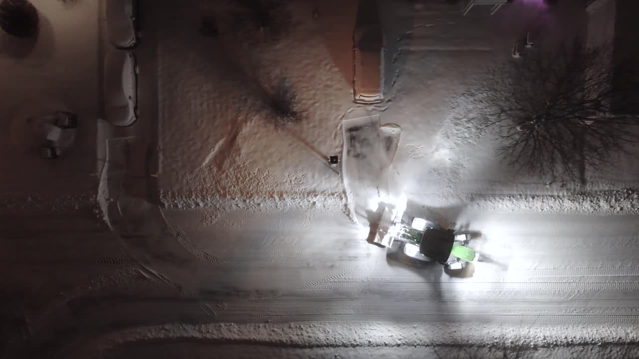 Bird's eye view drone shot of snowplow clearing snow at night in Saint-Constant, Québec, Canada