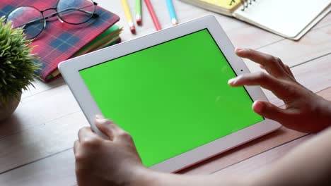 person using tablet with green screen on wooden desk