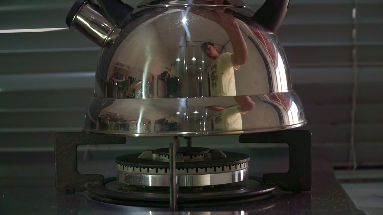 kettle sitting on gas stove ring, preparing to heat water, domestic kitchen cooking footage.