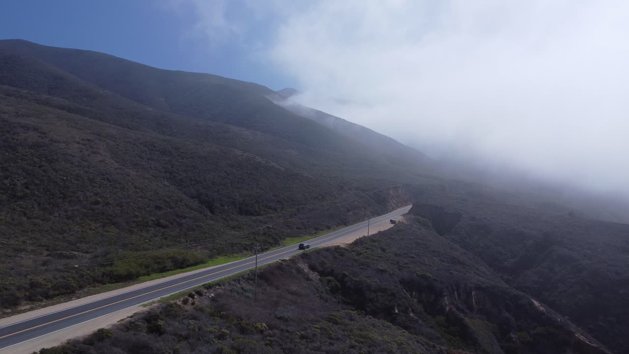 Drone shot of a road leading to a foggy mountain
