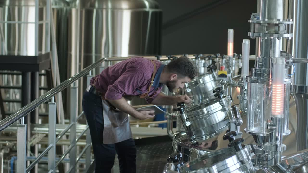 un joven cervecero con un delantal de cuero supervisa el proceso de fermentación de la cerveza en una fábrica de cerveza moderna