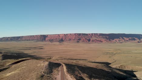 Toma-Aérea-De-Una-Carretera-Vacía-Que-Se-Adentra-En-Las-Rocas-Rojas-De-La-Montaña-En-El-Paisaje-Del-Cañón-En-El-Desierto-Seco