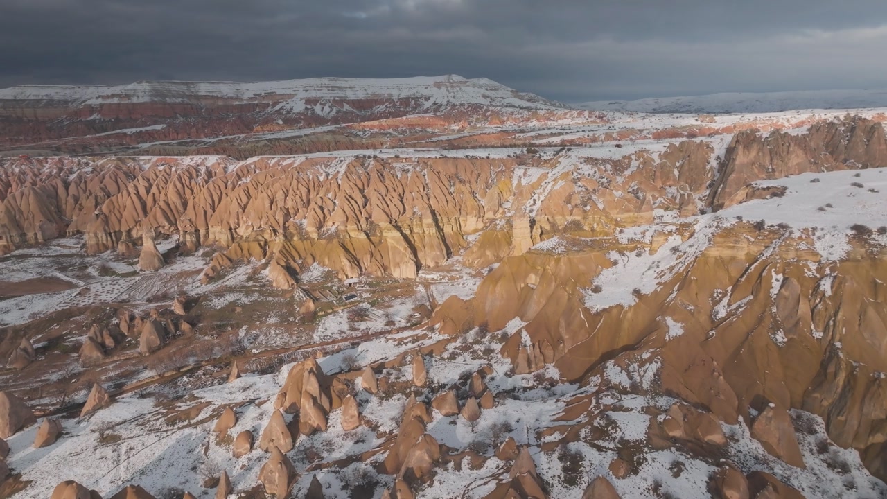 Aerial panorama of the Red Valley in Cappadocia, Turkey, during winter. Volcanic rock formations covered in snow at sunset, showing the unique geological landscape of Anatolia.