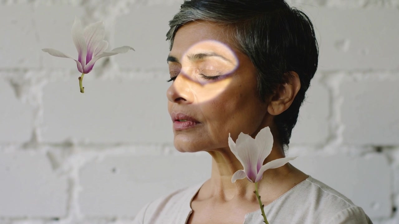 Donna seduta in camicetta chiara in posa accanto a un muro di mattoni, con la luce che accarezza due magnolie alla deriva.
