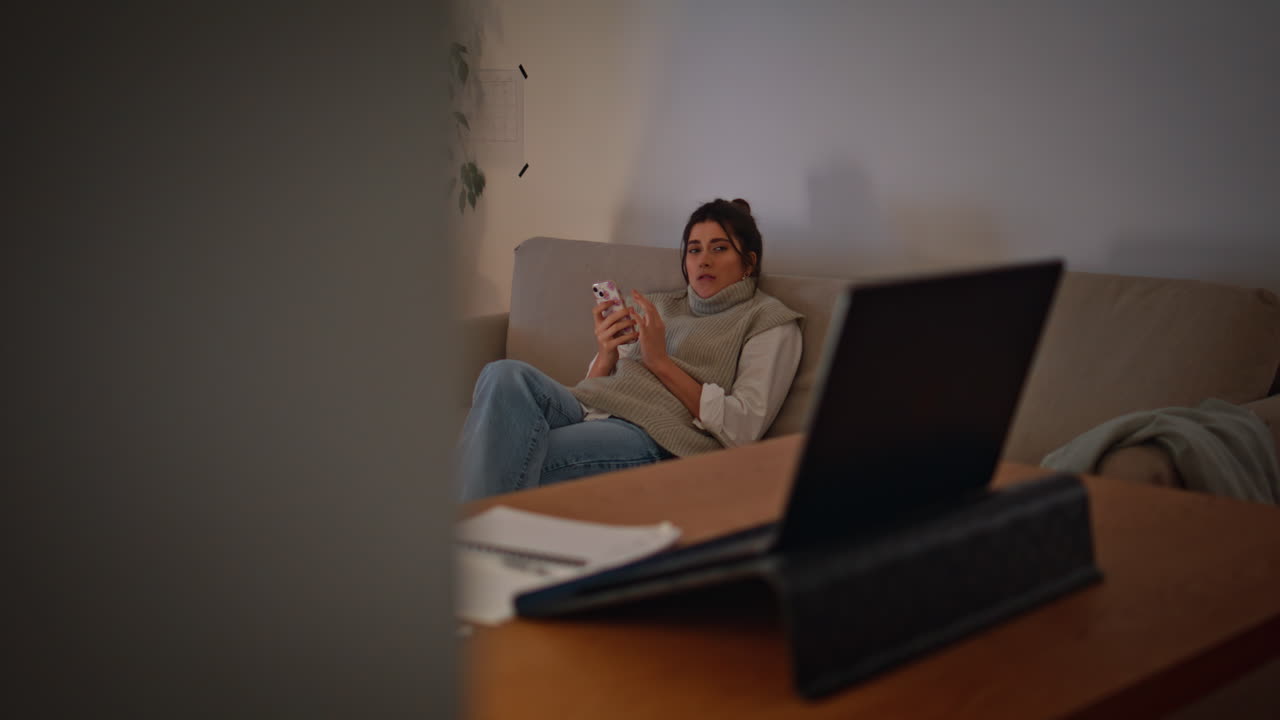 mujer relajada navegando por el teléfono inteligente en el sofá de la noche. dama comprobando el correo electrónico de la computadora portátil