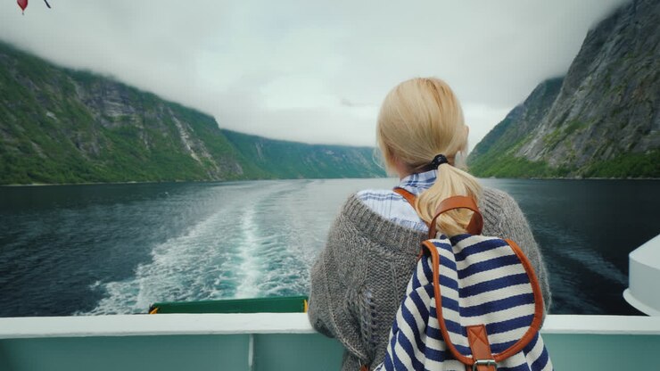 Touristinfrau bewundert den malerischen norwegischen Fjord vom Heck eines Kreuzfahrtschiffes