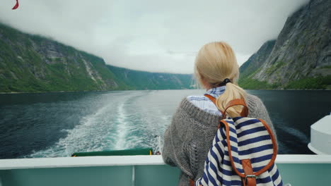 touristenfrau, die den malerischen norwegischen fjord vom heck eines kreuzfahrtschiffes aus bewundert