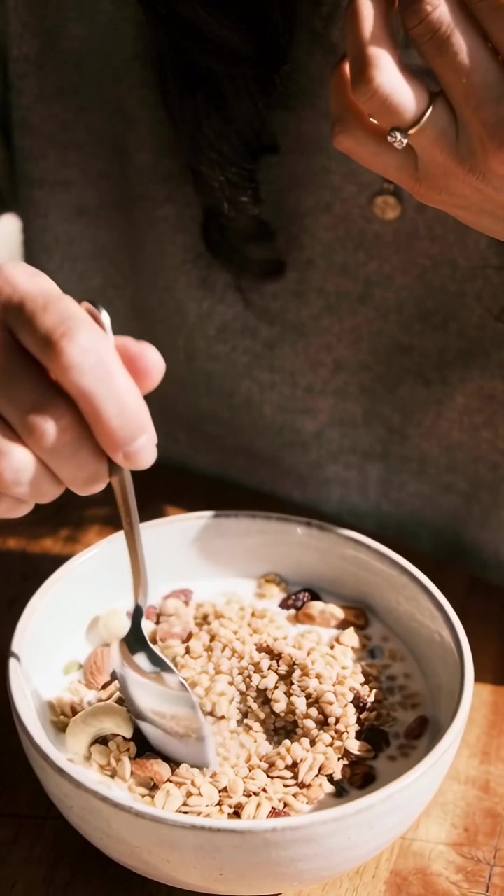 Video verticale: Mani che prendono un cucchiaio e mescolano muesli in una ciotola a casa, aggiungendo fragole.