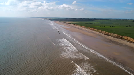 High-Establishing-Aerial-Drone-Shot-over-Fraisthorpe-Sandy-Beach-and-Calm-Waves-with-Green-Fields-Behind-on-Sunny-Day