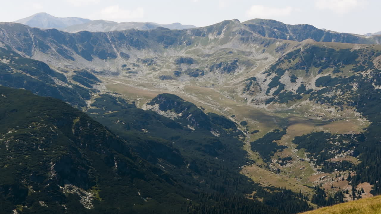Wide view zooming out and panning left across Transalpina mountains in bright daylight