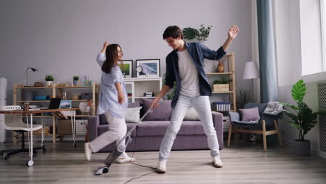 couple dancing with vacuum cleaners in living room