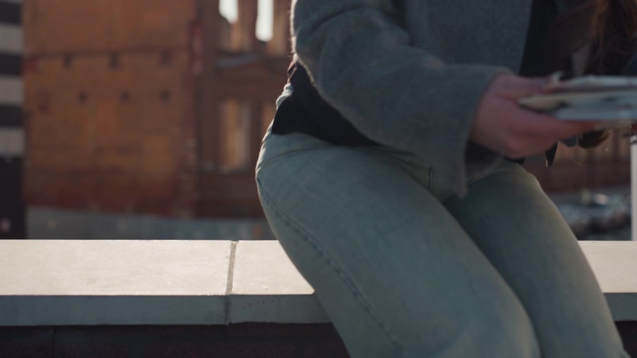 Pretty rooftop artist white woman sits, adjusts palette and prepares brush on ledge in denim, closeup of legs and hands, golden hour light on brick warehouse, intimate calm mood and thoughtful pause