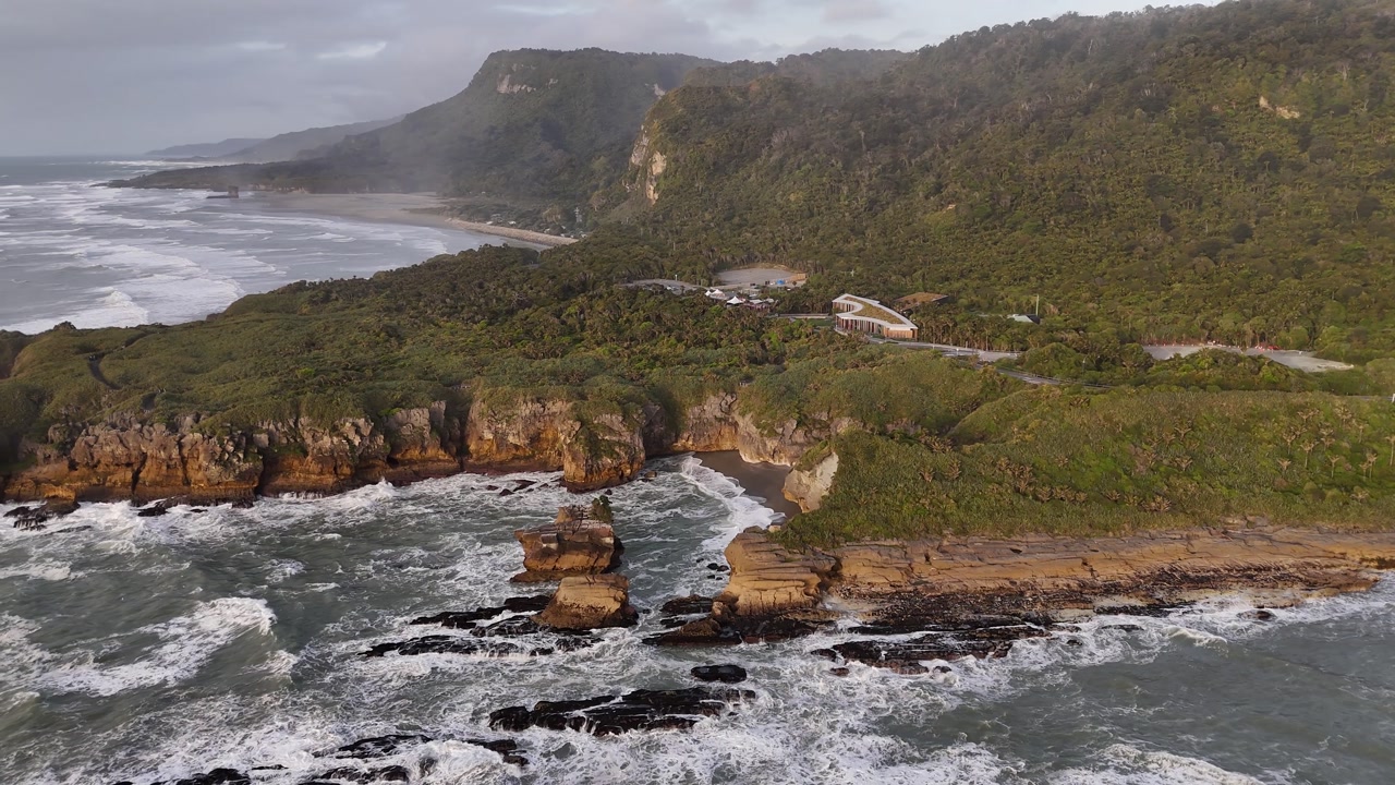 Drone boom up and dolly back movement smoothly reveals a stunning panoramic view of Pancake Rocks at sunset in Punakaiki on New Zealand