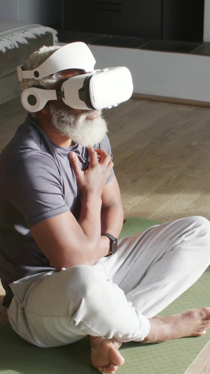 Video verticale: Reazione a un uomo in VR con maglietta grigia che indossa un visore VR, si tocca il petto su un tappeto verde a casa.