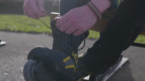 close up young man tying inline roller blade skates laces, golden hour evening sunset